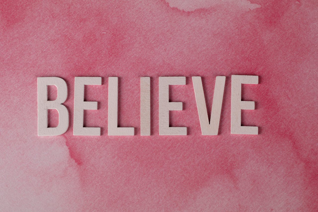 Inspirational word 'Believe' crafted on a textured pink watercolor background. Ideal for motivation.